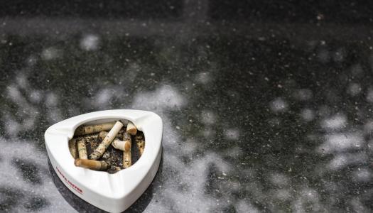 An ashtray with cigarettes sits on a gray floor. 